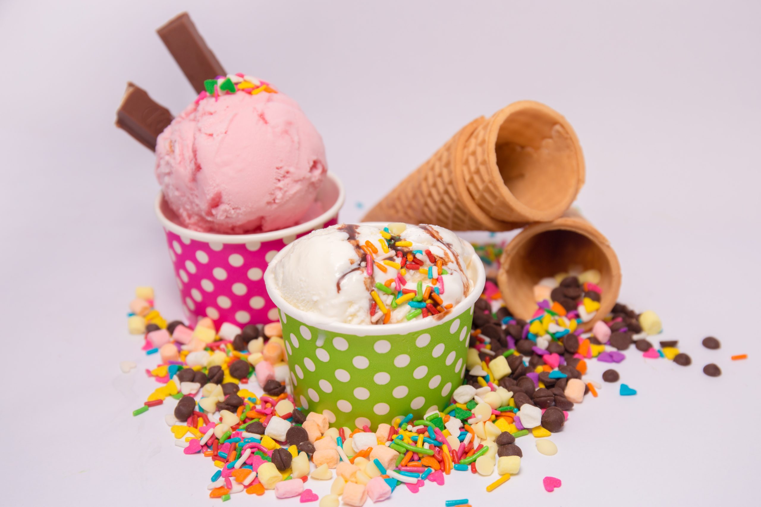Strawberry and vanilla ice cream in cups with sprinkles and cones